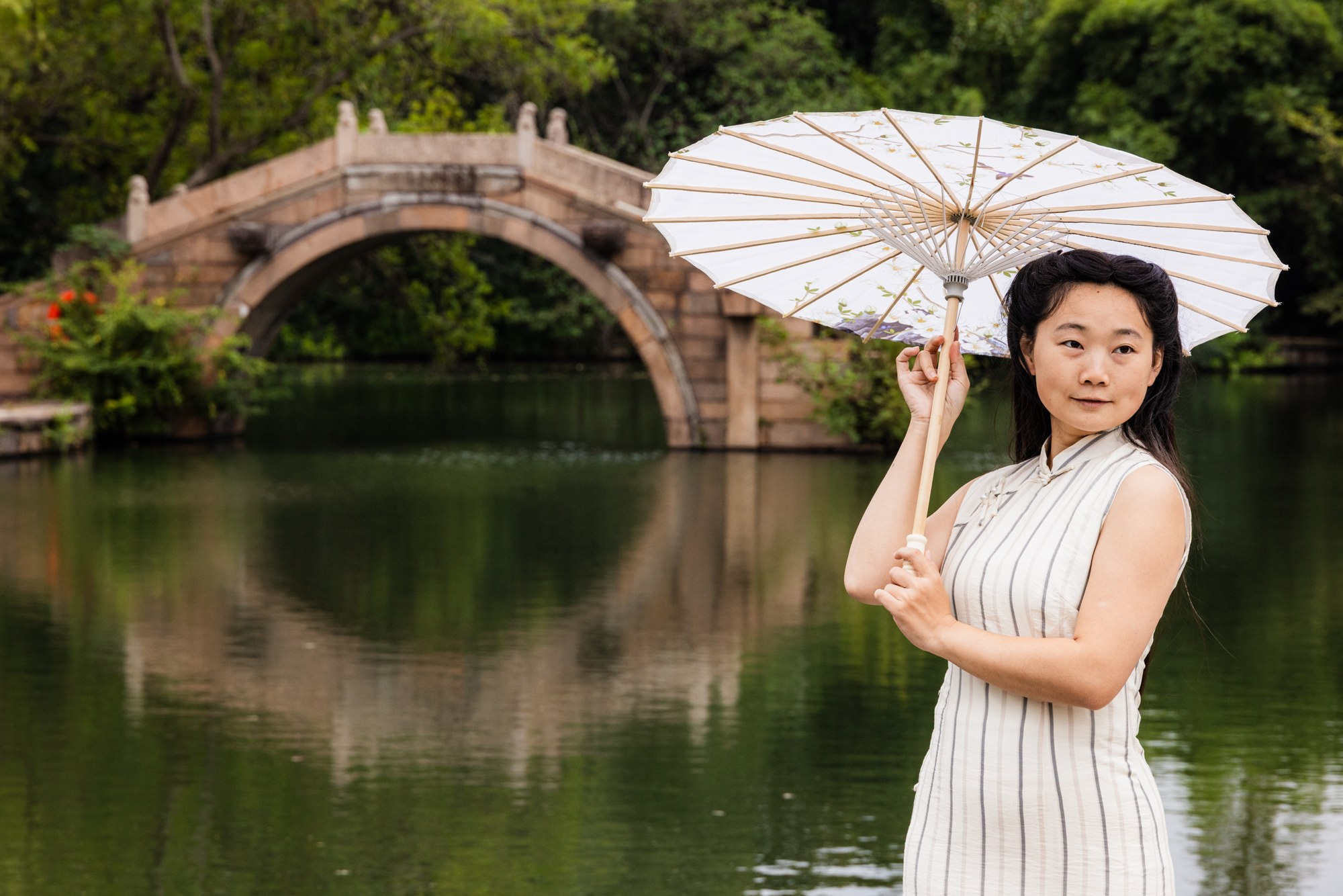 Vrouw in qipao met witte parasol bij de maanbrug, weerspiegeld in het water, China