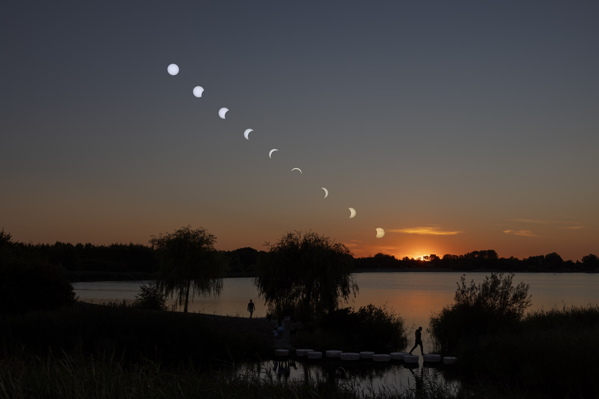 Negen standen van een gedeeltelijke zonsverduistering in een boog boven de Toolenburgerplas, met de ondergaande zon aan de horizon en een man die over de stapstenen loopt