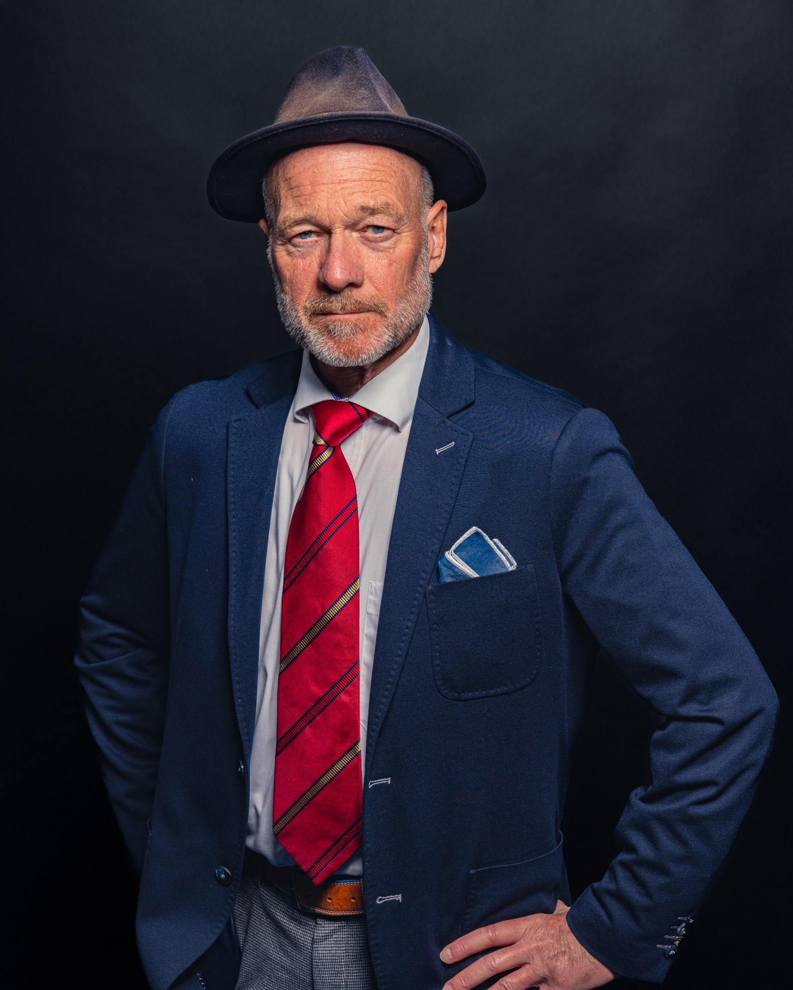 Man met fedora, marineblauw pak en rode das, staand karakterportret op zwart