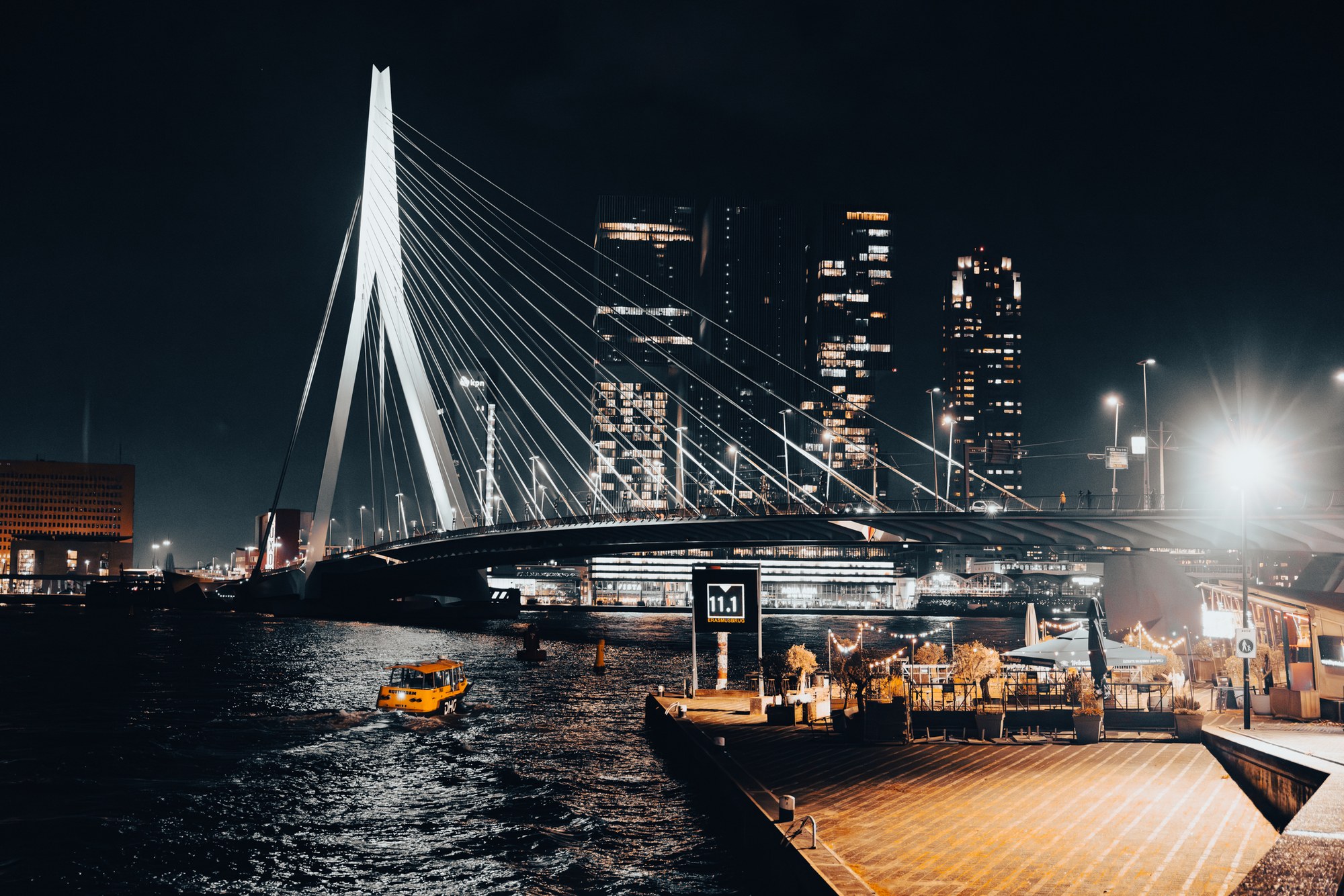 De Erasmusbrug en de skyline van Rotterdam bij nacht, weerspiegeld in het water