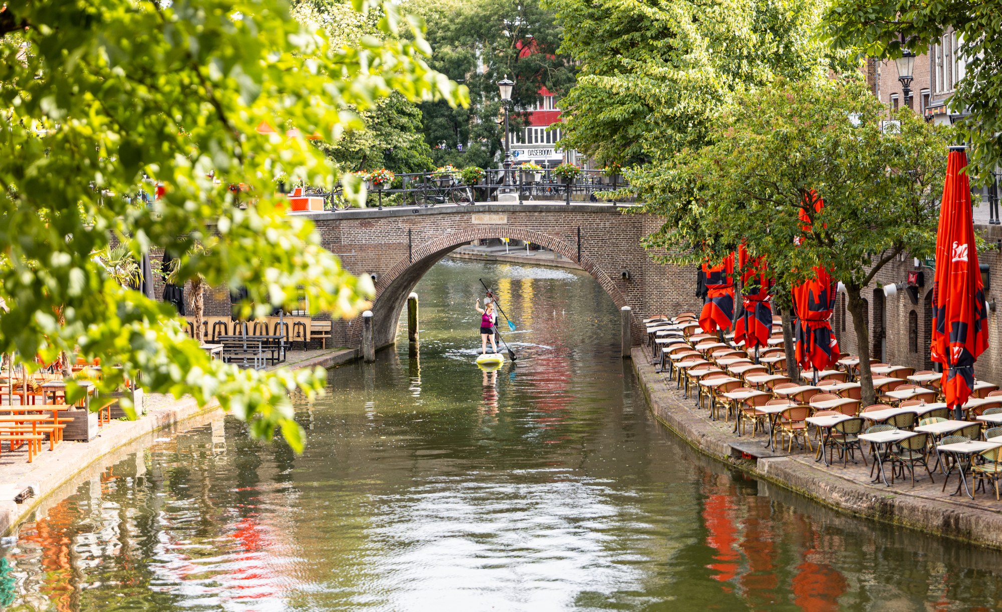 Utrechtse gracht met een SUP-peddelaar, rode parasols en een brug, Utrecht